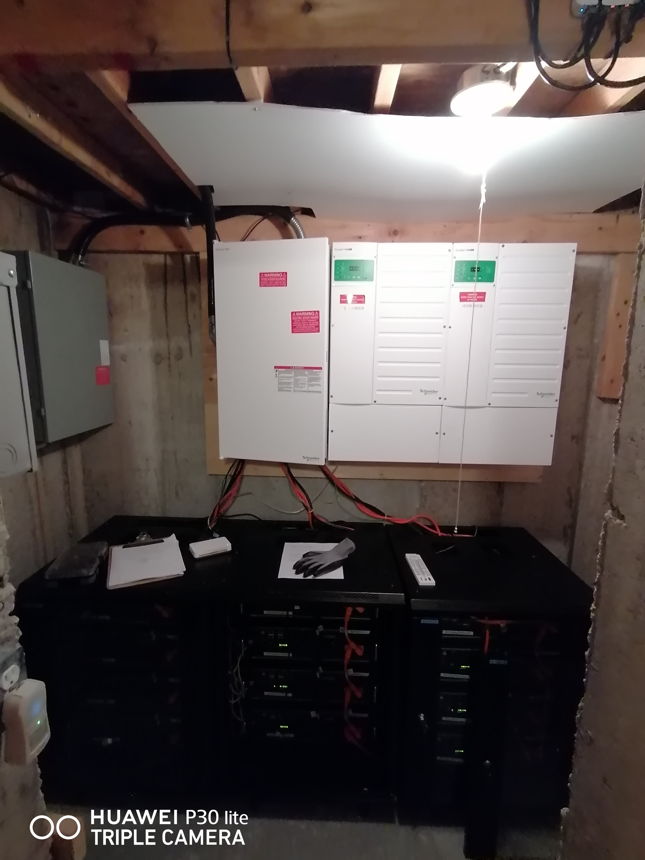 A storage room with electrical panels and black battery racks connected by red cables.
