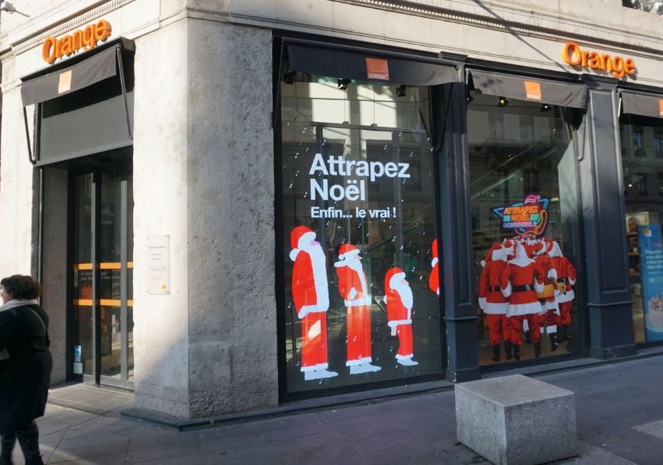 Vitrine d'un magasin Orange avec un écran LED transparent montrant des pères Noel
