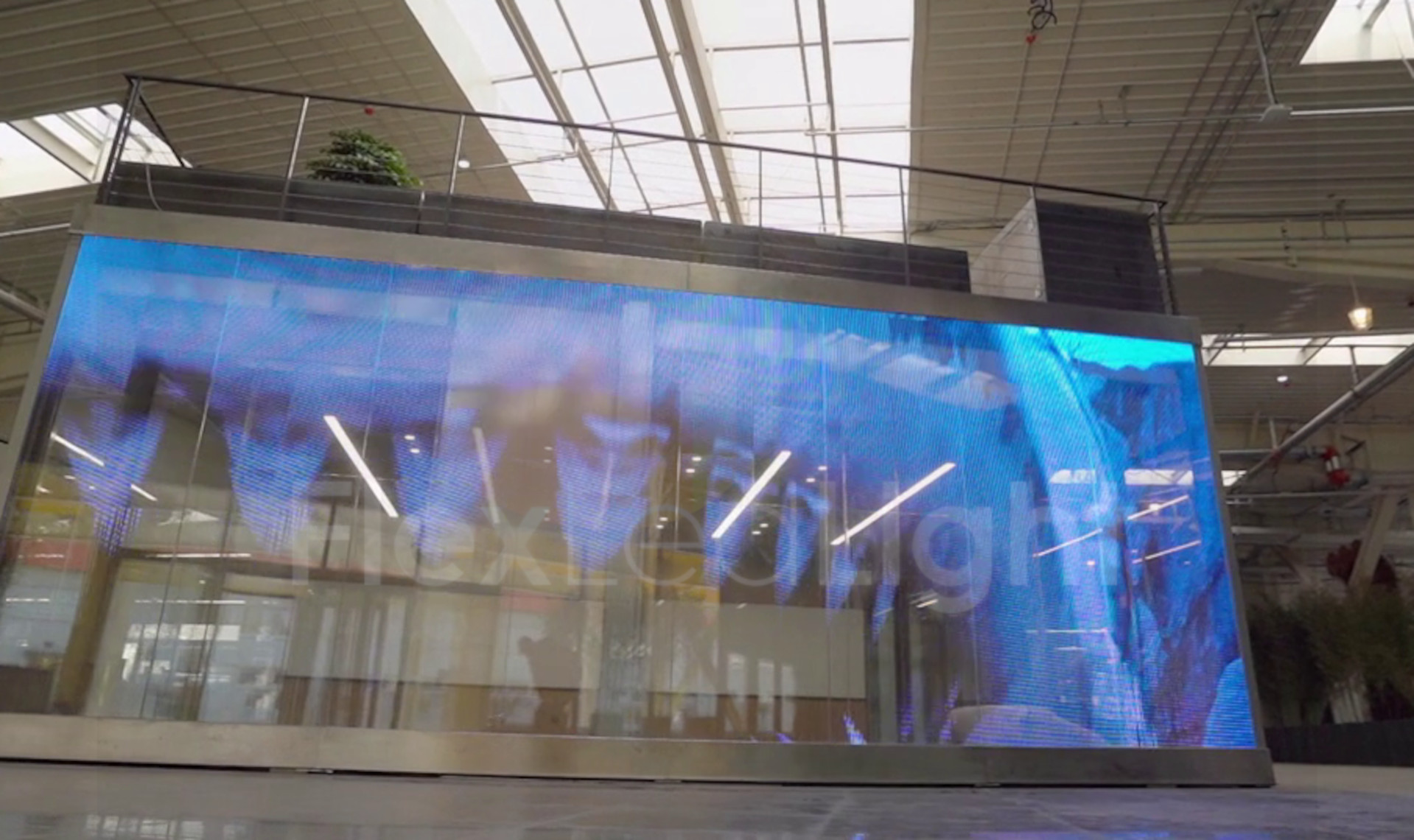 Écran LED géant intérieur dans un espace d’exposition, affichage lumineux bleu et image reflétée sur une paroi vitrée, sur une structure métallique. Esthétique moderne. consommation électrique écran led géant intégrée.