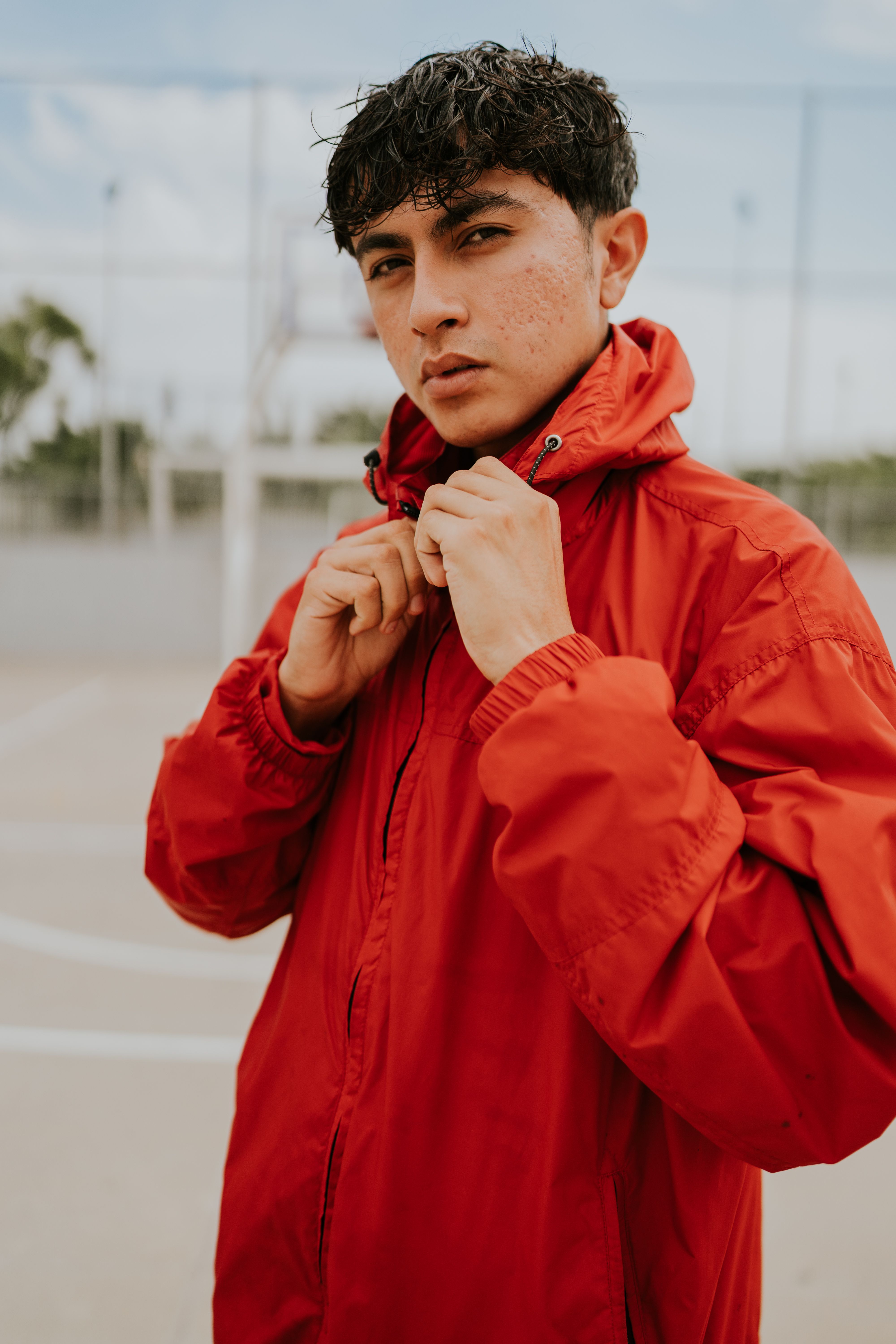 Homme portant une veste coupe-vent rouge à capuche, fermée par un zip, en extérieur