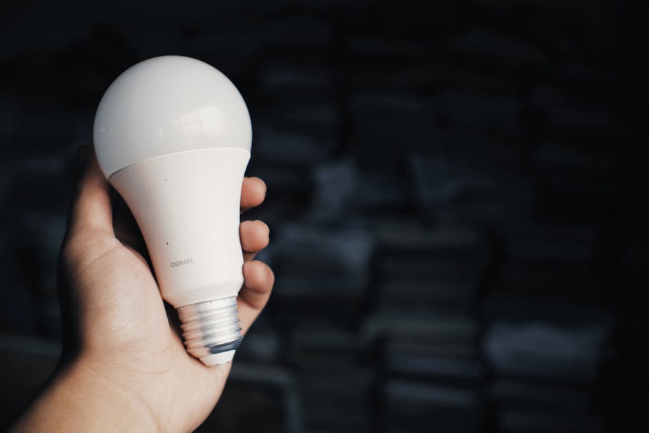 Gros plan d'une main tenant une ampoule LED à l'intérieur, avec un fond sombre.