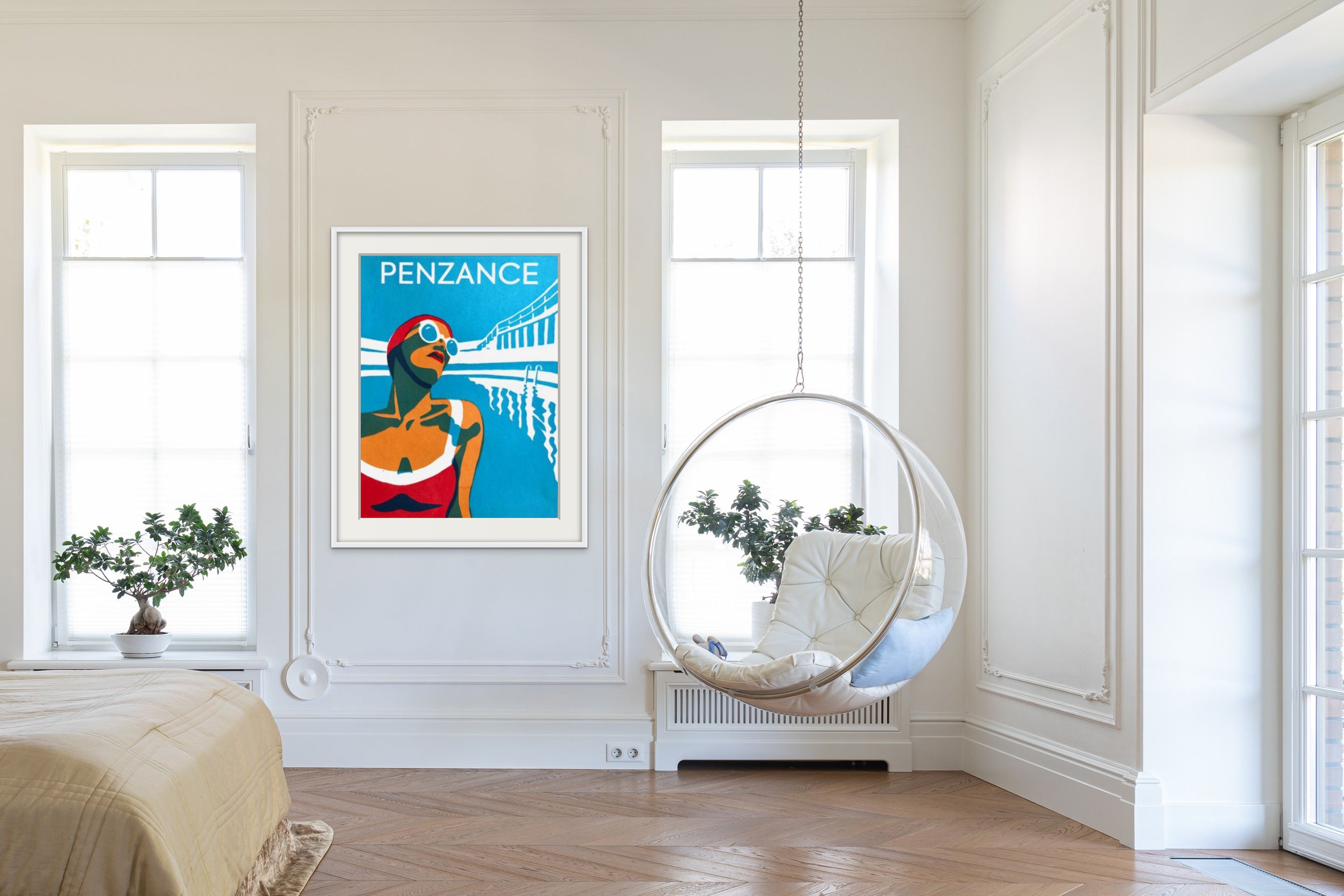 Bright, airy living room with white walls, a hanging circular chair, and a framed Penzance poster between two windows flanking a radiator.