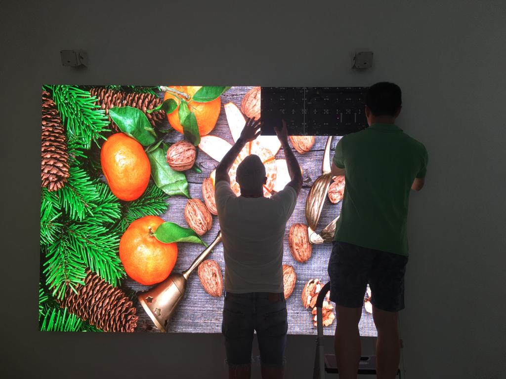 Écran LED géant en installation extérieur en cours de montage, deux personnes ajustant des modules lumineux contre un mur, affichage d’images fruits et noix.