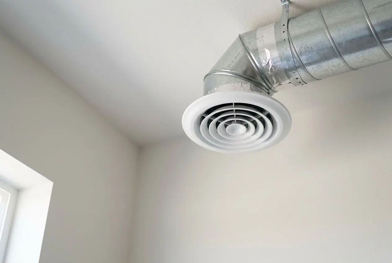VMC circulaire au plafond d’une pièce, raccordement métallique apparent et conduit demi-rond en aluminium. rt 2020 vmc double flux obligatoire