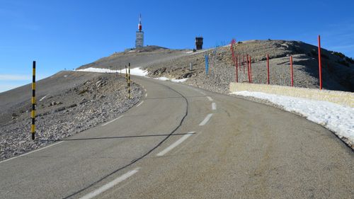 Piste routière sinueuse en montagne avec barrières et neige sur les contours, mont remontant sous un ciel bleu. Piste routière sinueuse en montagne avec barrières et neige sur les contours, mont remontant sous un ciel bleu.