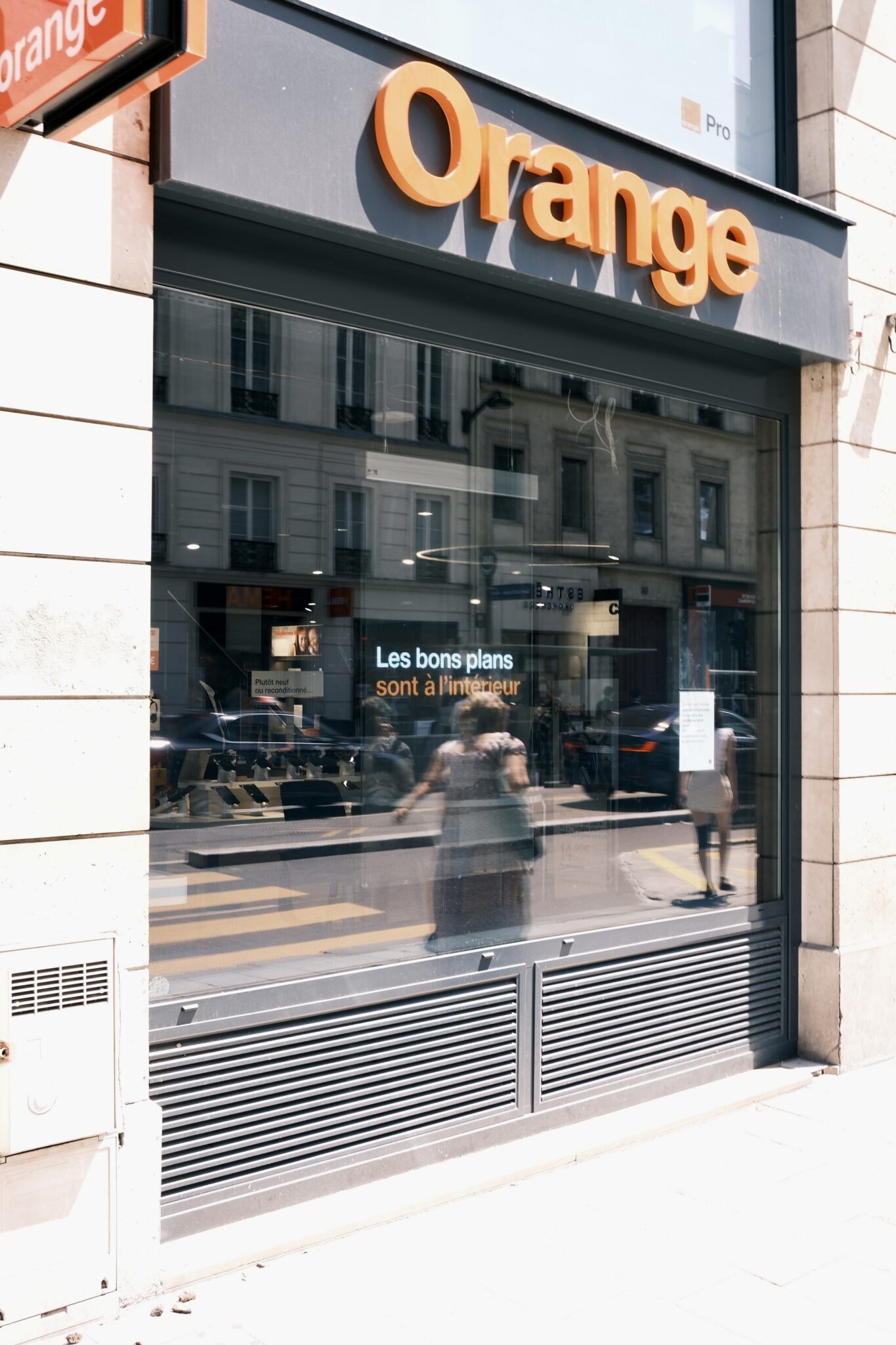 Facade d’un magasin Orange avec grande vitre sombre, reflet de rue et passants. alt: façade Orange, vitrine et enseigne orange, rue parisienne. Include keyword: "comment enlever l'eau de son écran" must integrate naturally. But image shows storefront; cannot force irrelevant. Must describe truthfully. We should try to integrate keyword if natural: "Façade Orange dans une rue, illustration d’un article sur comment enlever l'eau de son écran" but not claim content of page. It's alt text for image; include keyword if possible but not forced. We'll craft: "Facade du magasin Orange avec vitrine, illustration pour comment enlever l'eau de son écran." That's awkward but includes keyword. Keep 50-125 chars. Let's write: "Facade du magasin Orange avec vitrine, reflet des passants; sujet lié à comment enlever l'eau de son écran." That is okay. Ensure French. Let's output.
