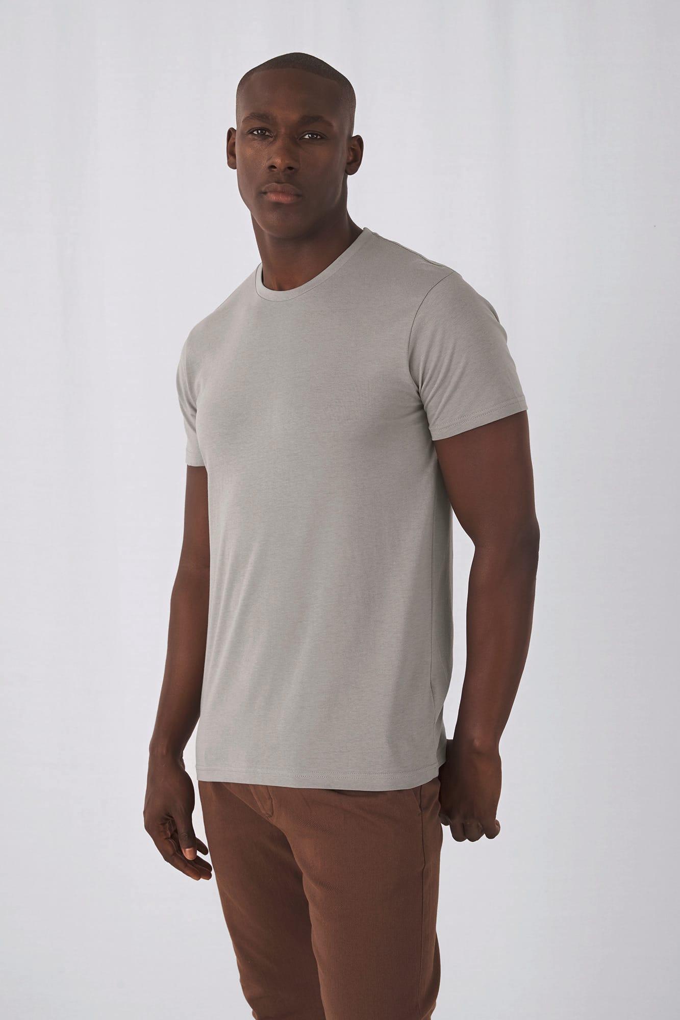 Homme portant un t-shirt gris simple, debout, face à l’objectif, contre un fond clair.